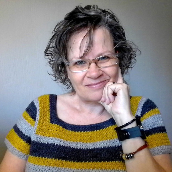 Smiling woman with short curly hair and glasses resting her chin on her hand, wearing the Sunflower Road Tee in stripes of mustard yellow, navy and light grey, with bracelets on her wrist.