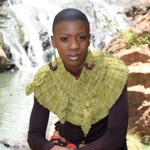 Leaves Cowl - A woman sitting in front of a waterfall wearing a green knit cowl with knit leaves attached.