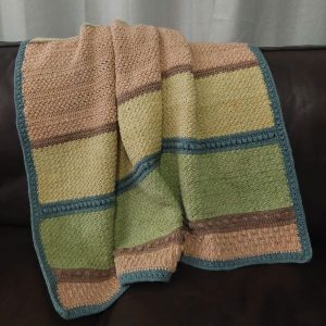 The Crumble Lapghan, crochet knee rug using textured stitches; draped over a leather couch.