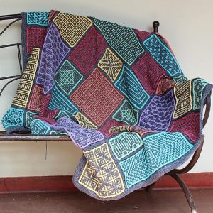 Wacky Weave Babette - a colourful blanket of interlocking crochet shapes, draped over a metal bench