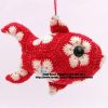 A crocheted fish toy hangs by string. The fish is red with white and pink hexagons. It has black button eyes and is crafted with textured crochet stitches.