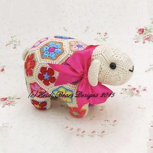 Kit for crocheted lamb soft toy made from colorful African flower motifs, featuring a cream head with black button eyes, embroidered mouth, and pink ribbon bow; handmade using vibrant hexagons and pentagons in floral designs—pattern by Heidi Bears Designs.