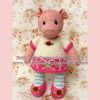 Hand-knitted pig toy in a whimsical outfit featuring a white dress with pink trim, striped blue leggings, and floral-accented pink shoes. Designed by Heidi Bears.