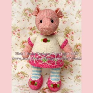Hand-knitted pig toy in a whimsical outfit featuring a white dress with pink trim, striped blue leggings, and floral-accented pink shoes. Designed by Heidi Bears.