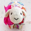 Close up of face of crocheted lamb soft toy made from colorful African flower motifs, featuring a cream head with black button eyes, embroidered mouth, and pink ribbon bow; handmade using vibrant hexagons and pentagons in floral designs—pattern by Heidi Bears Designs.