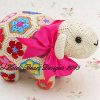 Close up of crocheted lamb soft toy made from colorful African flower motifs, featuring a cream head with black button eyes, embroidered mouth, and pink ribbon bow; handmade using vibrant hexagons and pentagons in floral designs—pattern by Heidi Bears Designs.