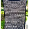 A hand‑knitted baby blanket held up outdoors, featuring intricate star and geometric motifs in white on a deep blue background.
