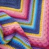 An intricately crocheted square blanket featuring layered rows of varied stitch textures in vibrant colours—blue, pink, purple, yellow, green, and red—displayed flat to show the pattern and craftsmanship