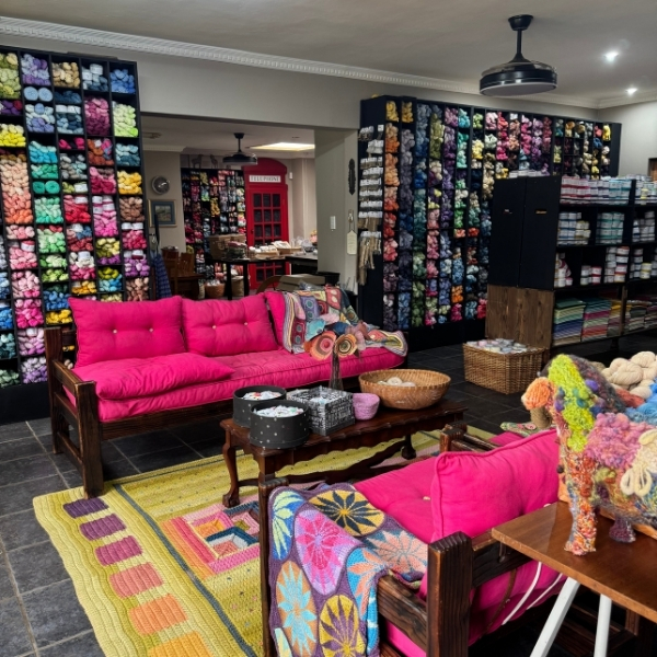 The ColourSpun studio, walls of hand dyed natural yarn arranged by colour on dark shelves, with colourful handmade textiles and pink couches in the foreground