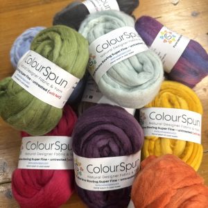 ColourSpun Pure Merino Roving Super Fine in a rich collection of hand dyed colours including olive, sage, charcoal, purple, crimson, mustard and orange, displayed on a wooden surface.