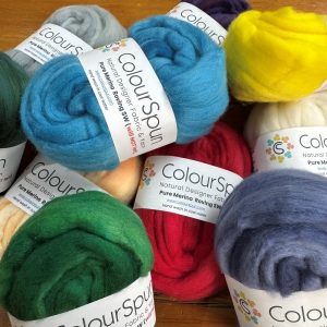 ColourSpun Pure Merino Roving Superwash in a vibrant collection of hand dyed colours including teal, red, green, yellow, grey, denim blue and cream, displayed on a wooden surface.