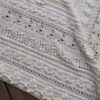 Close up of the border section of Mixology Edition 6 by Hooked on Sunshine, crocheted in Cotton Scintilla DK, draped over a wooden surface, showing alternating rows of bobble clusters, lace eyelets and textured stitch bands