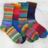 Four pairs of boldly striped hand knitted socks in ColourSpun Pure Merino Sock and 4ply yarn, showing vivid multicolour stripes in rainbow tones, laid together on a white surface.