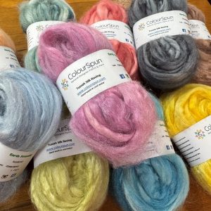 ColourSpun Tussah Silk Roving in a soft collection of hand dyed colours including pink, grey, blue, yellow, sage green and peach, displayed on a wooden surface.