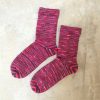 A pair of hand knitted socks in ColourSpun Pure Merino Sock and 4ply yarn, showing deep pink and charcoal tones in a fine stripe pattern, laid flat on a pale concrete surface.