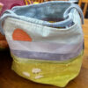 Close up of a pale blue project bag with an appliquéd sunset and hand embroidered sheep on a yellow green base.