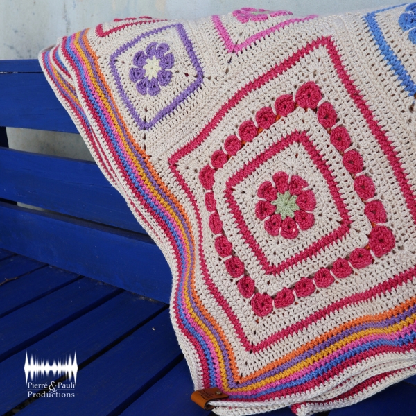 A close view of the Namaqua Blanket's diamond motifs in magenta, purple and blue, draped over the arm of a blue painted wooden bench