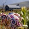 A close view of the Namaqua Blanket bundled in fynbos, showing the blue, orange, purple and magenta diamond patterns, with an old stone church blurred in the background