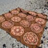 The Over the Coral Sea crochet blanket by Hooked on Sunshine in ColourSpun Pure Cotton DK, laid flat on a shell covered beach. Rows of round coral and cream mandala motifs are joined by caramel brown lacework and small raised roses.