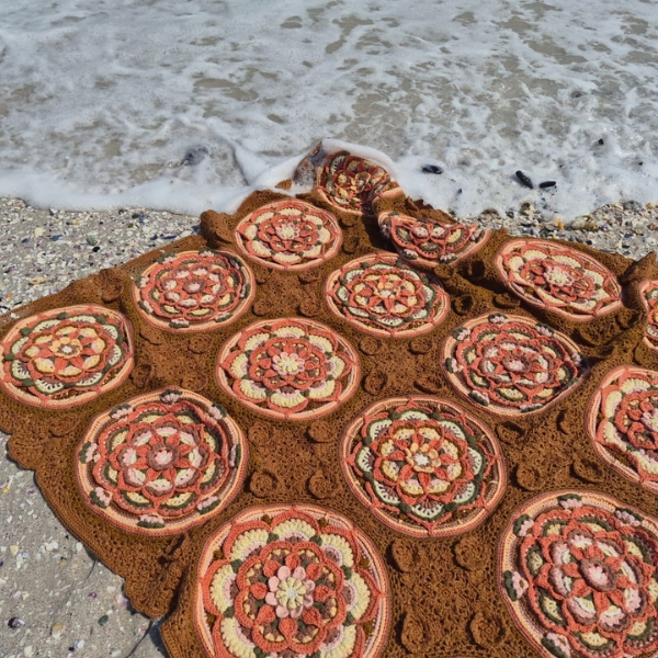 A wave washing up to the top edge of the Over the Coral Sea crochet blanket by Hooked on Sunshine, with coral, cream and green mandala motifs in warm caramel brown ColourSpun Pure Cotton DK.