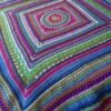 Multicoloured mandala square blanket crocheted in ColourSpun hand dyed yarn, laid diagonally across a bed
