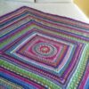 Full view of a crocheted mandala square blanket in ColourSpun hand dyed yarn, showing the striped border and colourwork