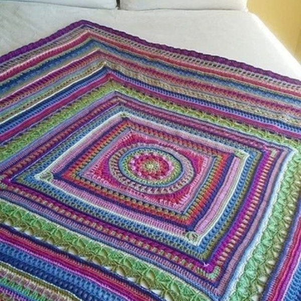 Full view of a crocheted mandala square blanket in ColourSpun hand dyed yarn, showing the striped border and colourwork