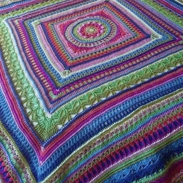 Multicoloured mandala square blanket crocheted in ColourSpun hand dyed yarn, laid diagonally across a bed