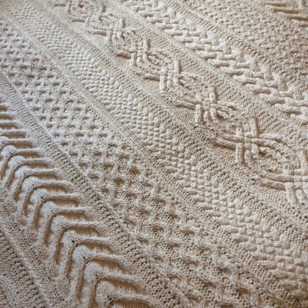 Close up of the Aran Caresse Cable Afghan by Hilda Steyn showing a twisted cable panel beside lattice and braided panels in cream