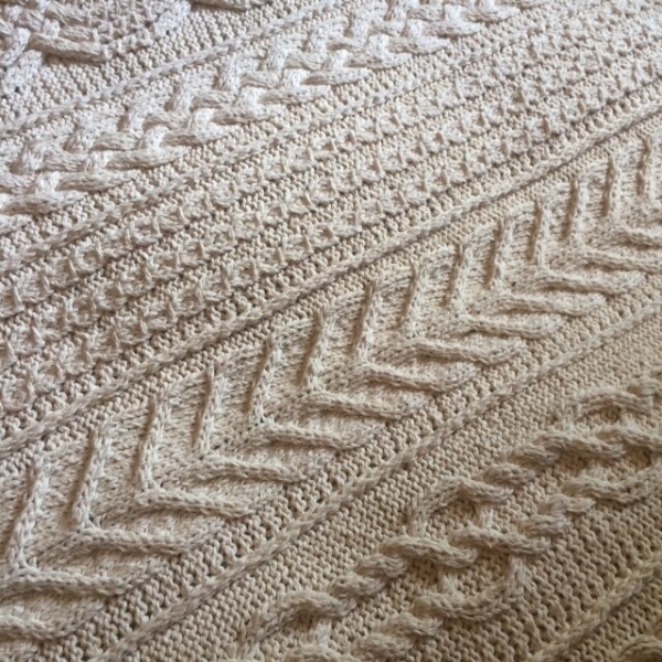 Detail of the Aran Caresse Cable Afghan showing a chevron panel and a braided cable panel in natural cream yarn