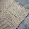 Cream cotton sample square from the Aran Caresse Cable Afghan Collection with a cable panel and a textured stitch, resting on grey patterned fabric