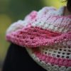 Close up of the Ireland Shawl draped over a shoulder, showing pink and cream stripes in clusters of crochet stitches and open mesh.