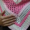 Close up of a hand resting on the Ireland Shawl, showing the open mesh, the raised puff stitches and the pink and cream stripes.