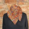 Close view of a hand dyed orange, green and purple shawl wrapped around the neck, with eyelet lines and a scalloped edge