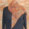 Hand dyed shawl in orange, green and purple, pinned at the shoulder with a wooden shawl pin, with one long point hanging down the front