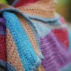 Close up of the Wild Winds Shawl folded over, showing turquoise and peach stripes with a grey edging beside panels of purple and red.