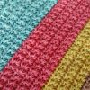 Close up of a crochet blanket in a textured star stitch, with diagonal bands of turquoise, coral pink and mustard yellow.