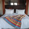 Striped crochet blanket in turquoise, pink, yellow, orange, sage and tan draped diagonally across a white bed with a tufted leather headboard.