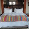 Colourful vertical striped crochet blanket with a dusty pink border laid across the foot of a white hotel style bed.