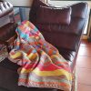 Brightly striped crochet blanket in yellow, pink, orange, sage and blue draped over a brown leather armchair on a terracotta tiled floor.